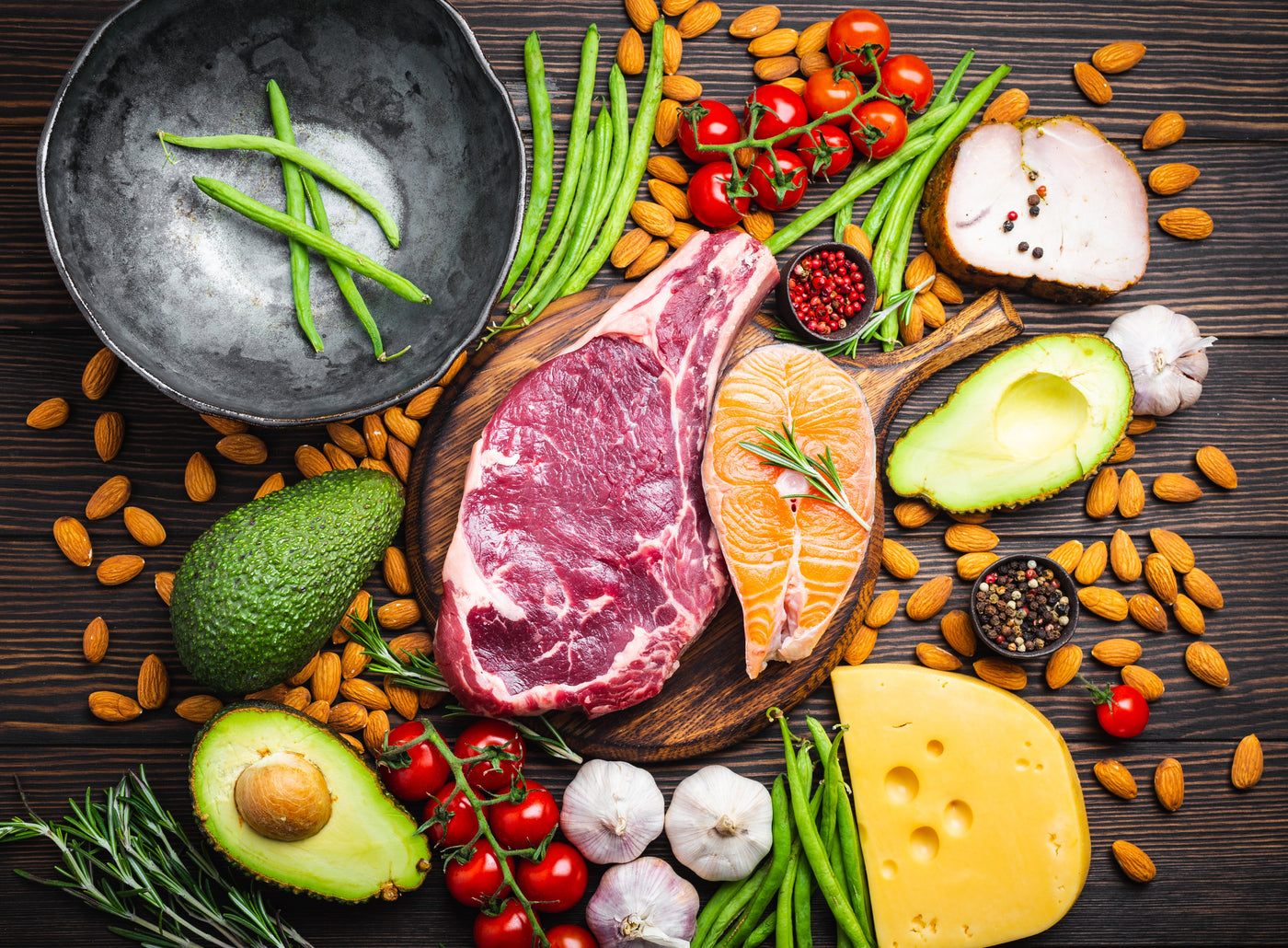 Paleo spread on wood table with cherry tomatoes, lentils, avocados, french beans, garlic, asparagas and cheese.