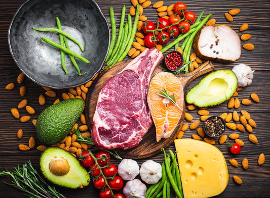 Paleo spread on wood table with cherry tomatoes, lentils, avocados, french beans, garlic, asparagas and cheese.