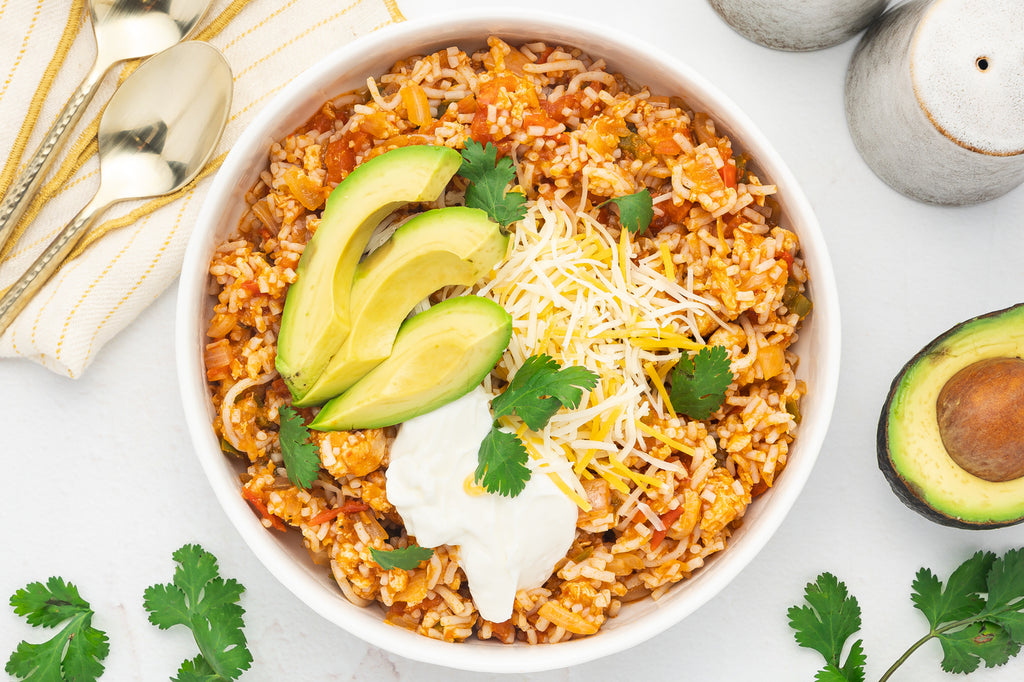 An overhead image of a chicken taco bowl made with rice and garnished with fresh cilantro, sour cream, and sliced avocado.