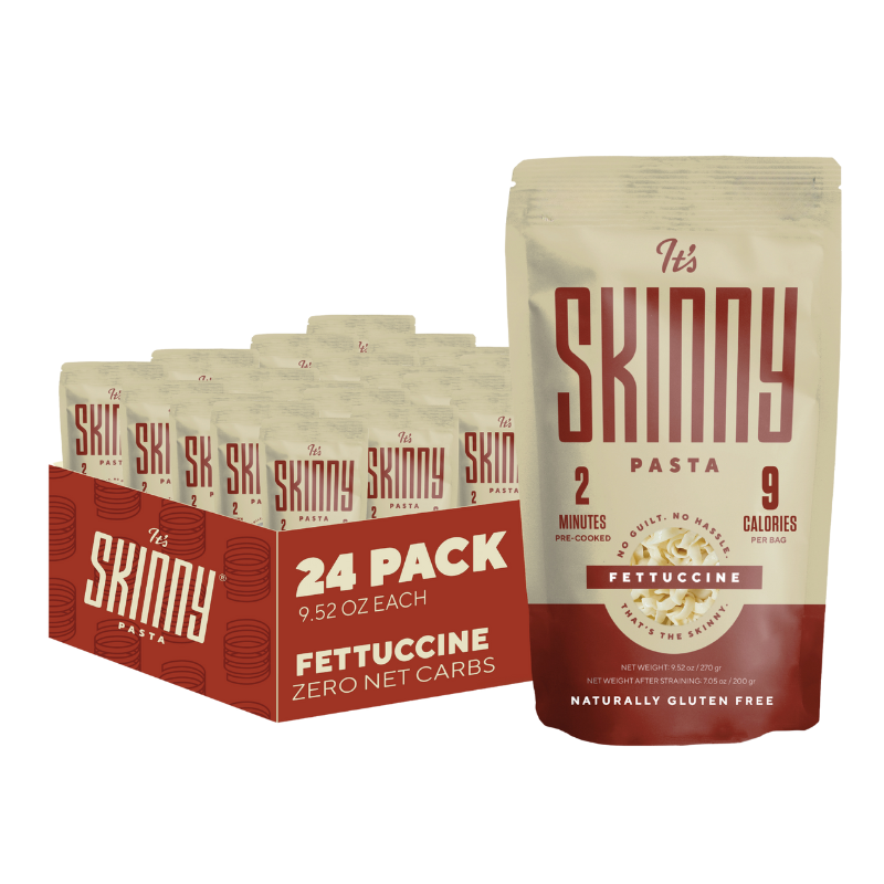 A cream and maroon package of It's Skinny Fettuccine Pasta stands in front of a 24 pack of pasta.