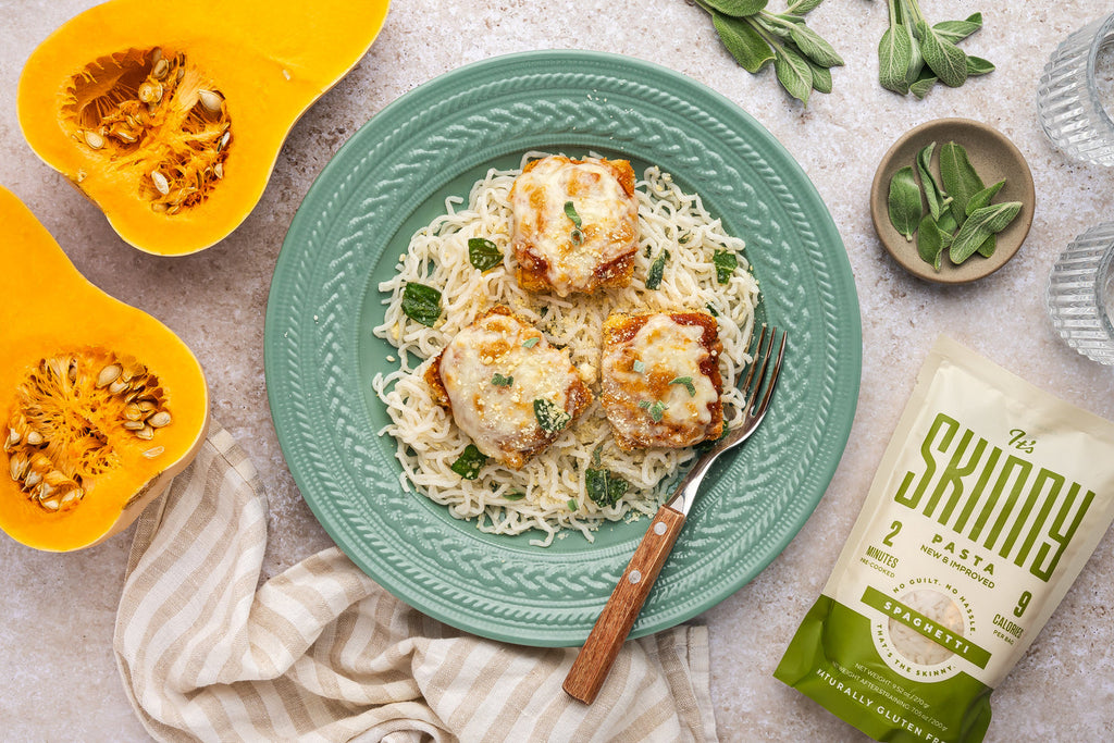 A bowl of Creamy Butternut Squash Pasta with It's Skinny Spaghetti Pasta on a turquoise platter. Dish is placed in between two halves of butter nut squash and It's Skinny Spaghetti packaging.