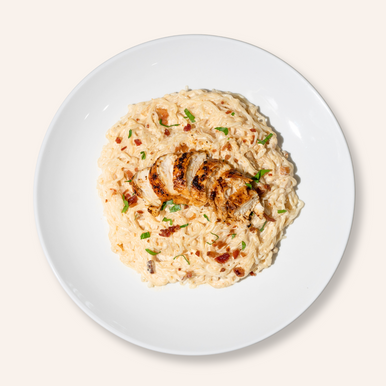 An overhead image of a bowl of It's Skinny Organic Angel Hair Pasta prepared in a creamy sauce, topped with sliced chicken breast.