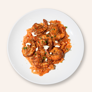 An overhead image of a dish of It's Skinny Organic Fettuccine Pasta cooked in a red sauce and topped with seasoned shrimp.